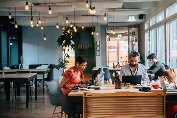 A modern office space with multiple workstations, hanging light bulbs, and large windows. - Appartements By Stay At (Basel)
