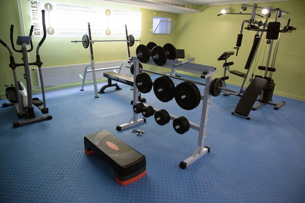 Un gimnasio con diversos equipos de ejercicio, como mancuernas, un banco y estanterías para pesas.