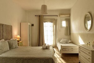 Quarto com uma cama grande, uma cama menor, cômoda, espelho e ar-condicionado.