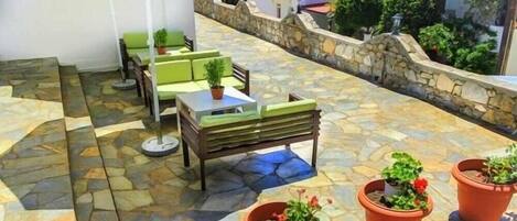 An outdoor patio area with stone flooring, green seating, and potted plants.