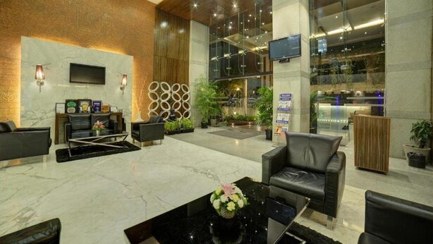 A modern lobby with a marble floor, leather seating, a flat-screen TV, and a reception desk. - Goldfinch Hotel Mangaluru (Mangaluru)
