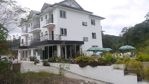 A multi-story white building with balconies, potted plants, and outdoor umbrellas. - Rovers Inn Tanah Rata (Tanah Rata)
