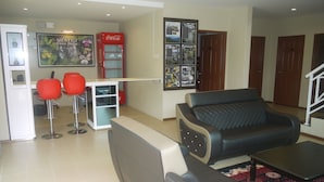 A modern living room with a sofa, a small table, and a red Coca-Cola refrigerator. There are two red chairs and a white cabinet. - Rovers Inn Tanah Rata (Tanah Rata)