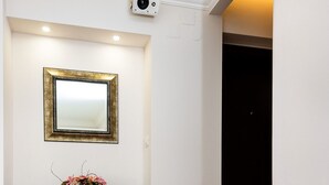 A hallway with a red carpet, a white wall, a dark wooden console table, a gold-framed mirror, and a small vase with pink flowers. - Meridien Luxury Apartments (Zagreb)