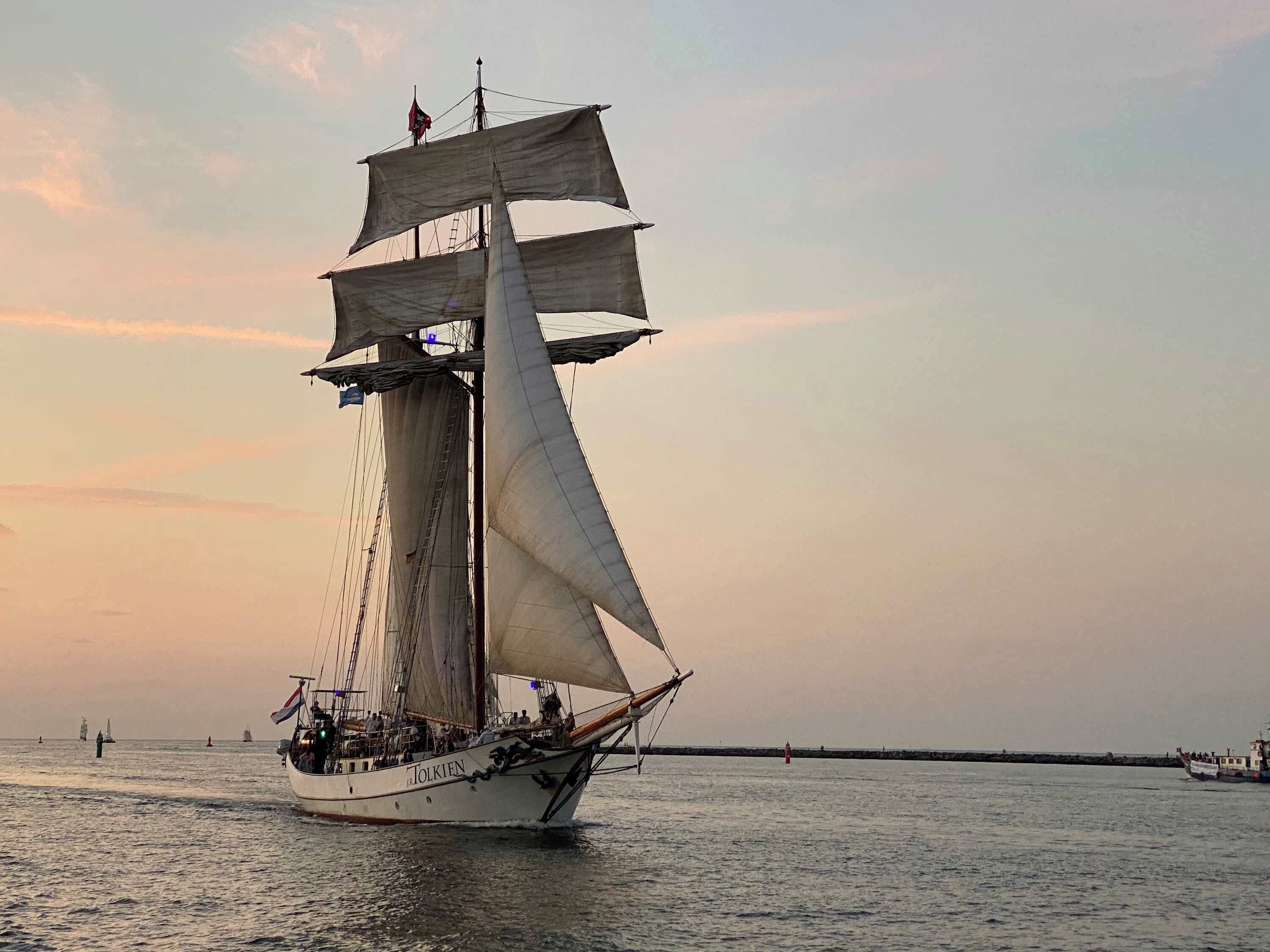 Un barco de gran altura con numerosas velas navegando sobre aguas tranquilas durante el atardecer.