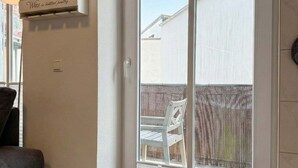 A room with a sliding glass door leading to a backyard, a clock on the wall, and a shelf with bottles and a sign.