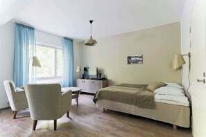 Een kamer met een bed, bureau, stoel, televisie en een raam met gordijnen.