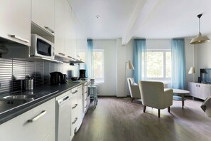 Een moderne keuken met een magnetron, koffiezetapparaat en waterkoker, een eethoek met een tafel en stoelen, en een televisie op een kast.