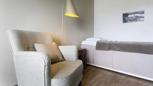 A room with a single armchair, a bedside table, a bed with a white headboard, a floor lamp, and a black and white photo on the wall. - Sato Hotelhome Kamppi (Helsinki)