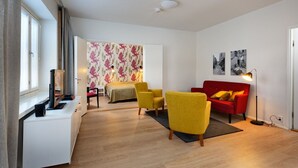 Una sala moderna con un sofá rojo, sillones amarillos, una mesita blanca y una cama con papel tapiz floral.