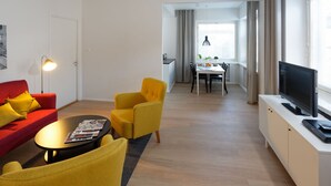 Una sala moderna con un sofá rojo, sillones amarillos, una mesa de centro redonda y un televisor sobre un mueble blanco.