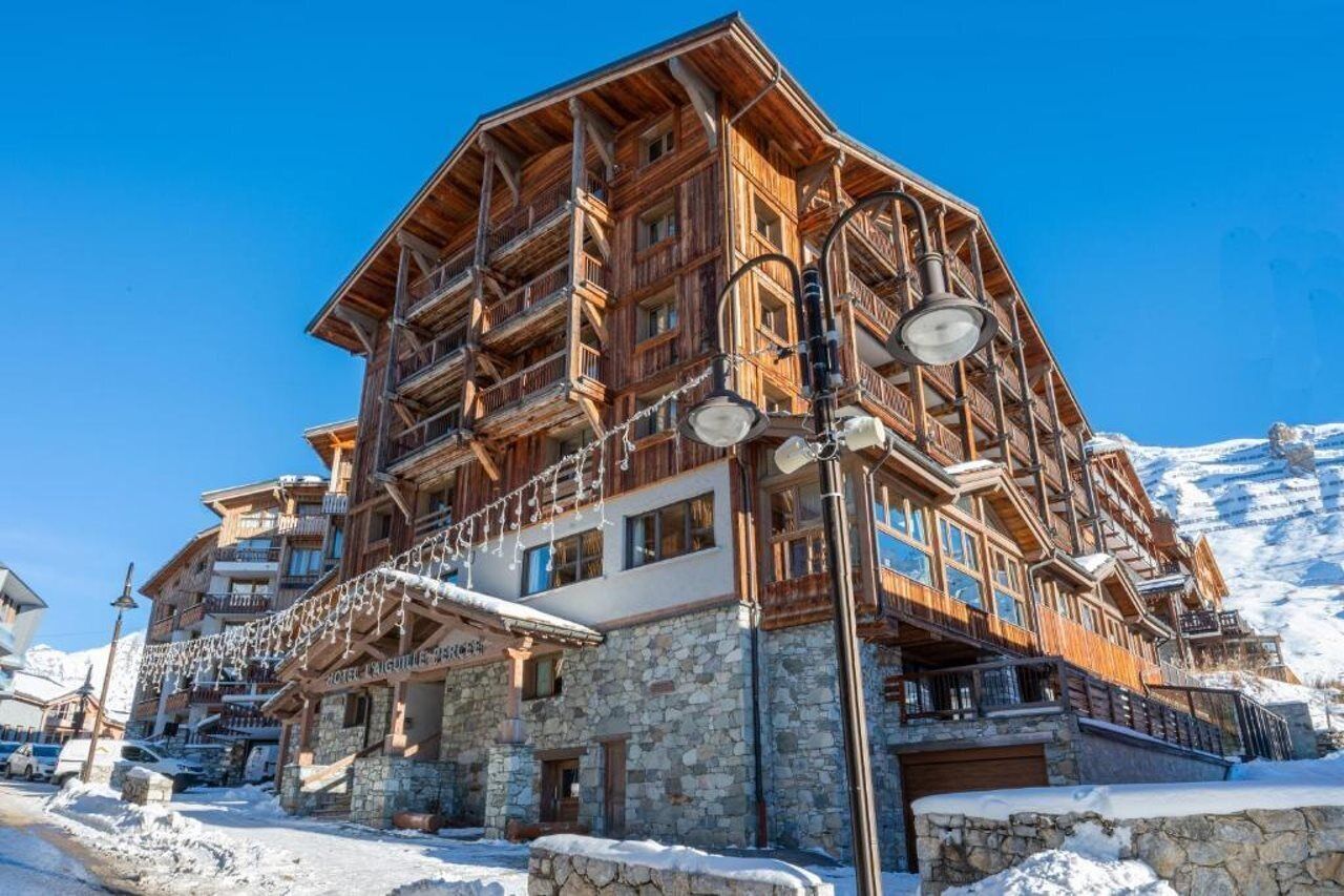 Un chalet en bois à plusieurs étages, doté de balcons, de fondations en pierre et situé à proximité d’un télésiège.