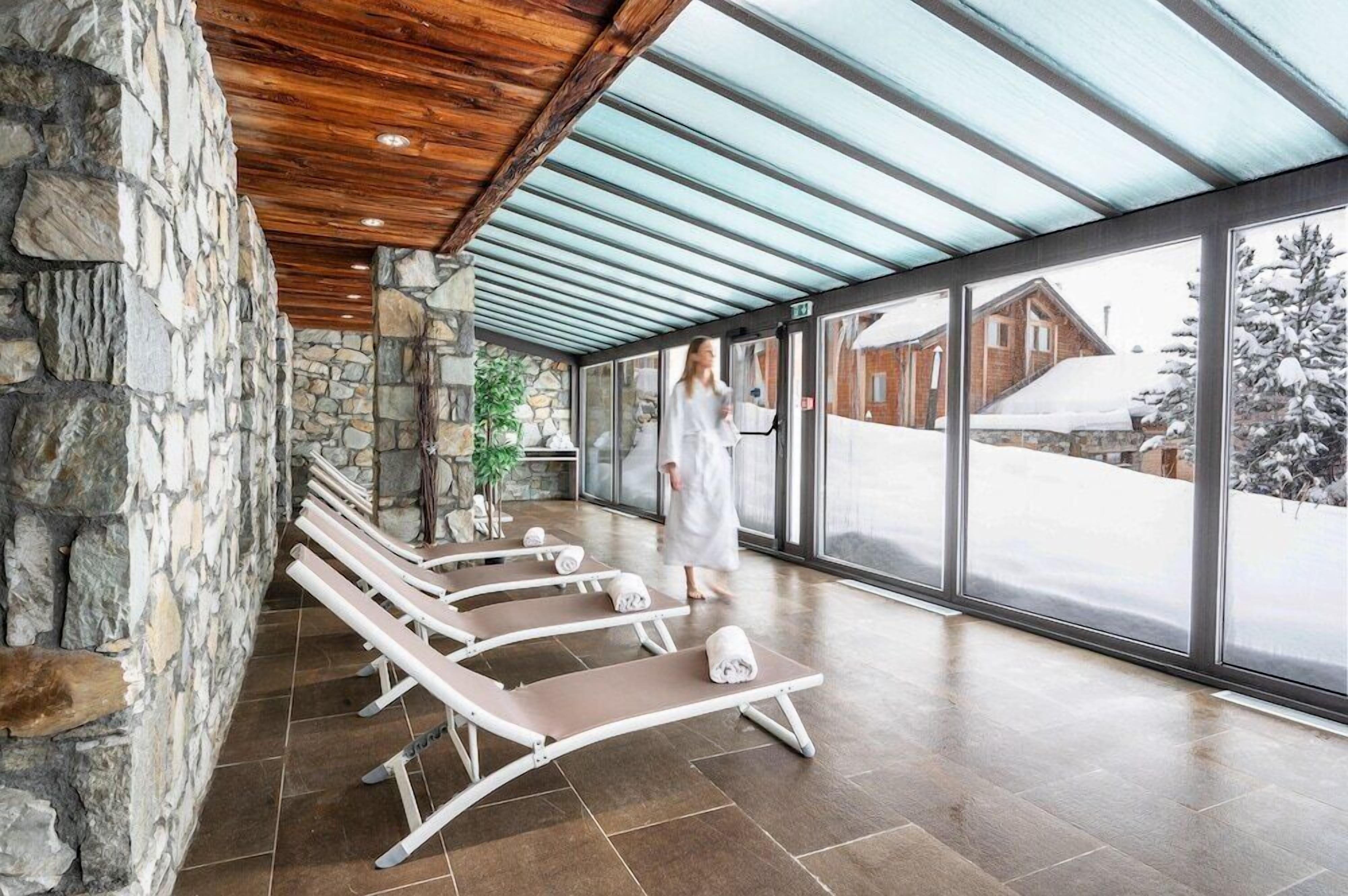 A spa area with stone walls, wooden ceiling, and glass doors leading to a snowy landscape.