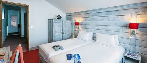 Une chambre d’hôtel avec une tête de lit en bois, un lit avec du linge de maison blanc, une table de chevet avec une lampe et une moquette rouge.