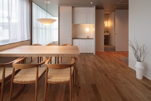 Un comedor moderno con una mesa y sillas de madera, una cocina al fondo y vistas a la ciudad a través de amplios ventanales.