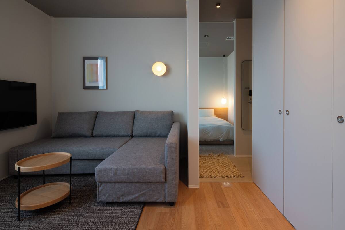 A modern living room with a grey sectional sofa, a wooden side table, and a flat-screen TV mounted on the wall.