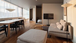 A modern living room with a wooden dining table, a sofa, and a TV mounted on the wall. - goodroom hotel Kyoto (Kyoto)