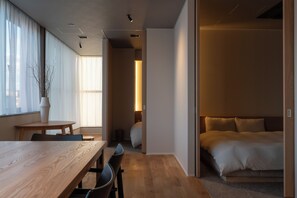 Una habitación moderna con una mesa de comedor de madera, una cama con edredón color beige y un pequeño rincón de descanso.