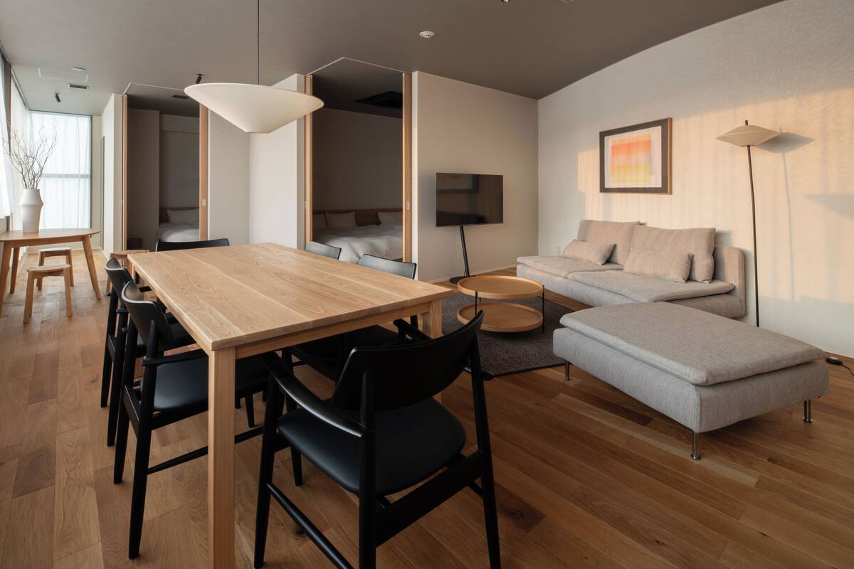 A modern living room with a wooden dining table, black chairs, a grey sofa, and a small round coffee table.