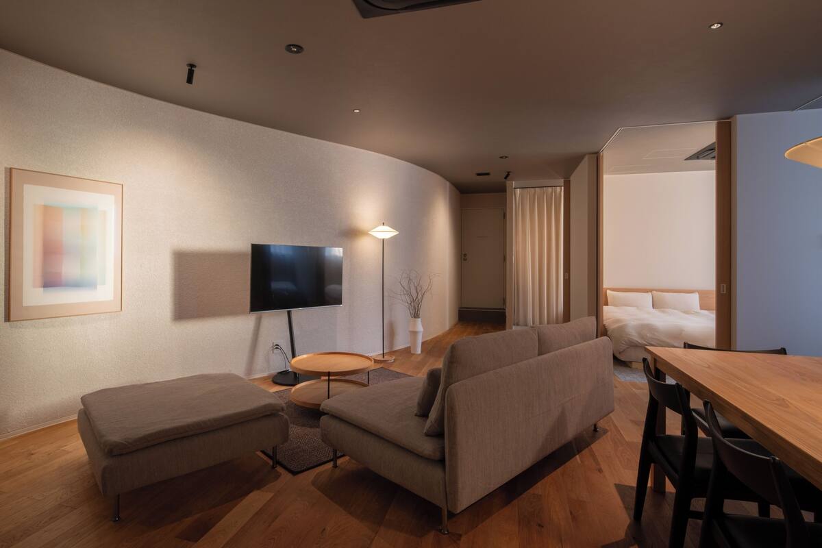 A modern living room with a sofa, a TV, a dining table, and a small round table.