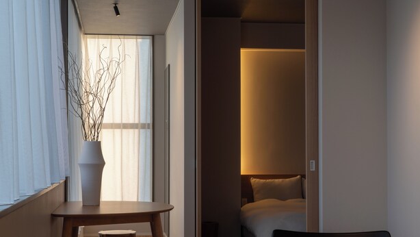 A modern hotel room with a wooden dining table, two chairs, a potted plant, and a bed with a headboard. - goodroom hotel Kyoto (Kyoto)