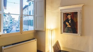 Una habitación con ventana a la calle, un radiador, una lámpara y un cuadro en la pared.