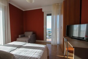 Une chambre d’hôtel avec un lit, une chaise, une télévision et un balcon avec des rideaux.