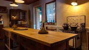 Une cuisine avec un îlot central en bois, des luminaires suspendus, une cuisinière et une fenêtre ornée de rideaux en dentelle.