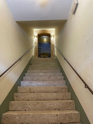 Una escalera de piedra con escalones que conducen a un rellano con una lámpara y un detalle decorativo en la pared.