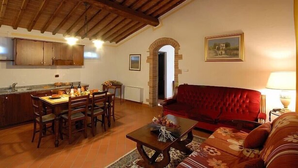 A cozy living area with a dining table, chairs, a red sofa, and a coffee table. - Fattoria Agriturismo Il Colombaio (Monteriggioni)