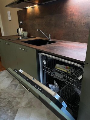 Una cocina moderna con lavavajillas integrado, pileta de acero inoxidable y extractor.
