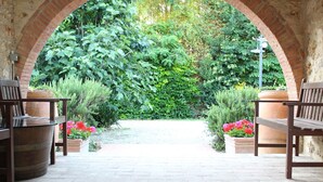 An outdoor garden area with brick arches, wooden benches, and potted plants. - Fattoria Agriturismo Il Colombaio (Monteriggioni)