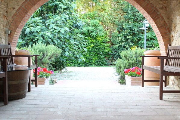 Un jardín al aire libre con arcos de ladrillo, bancos de madera y plantas en macetas.