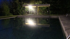 Una piscina con zona cubierta y reflejos de luces en el agua.