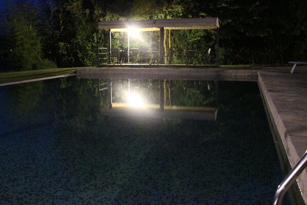 Una piscina con zona cubierta y reflejos de luces en el agua.