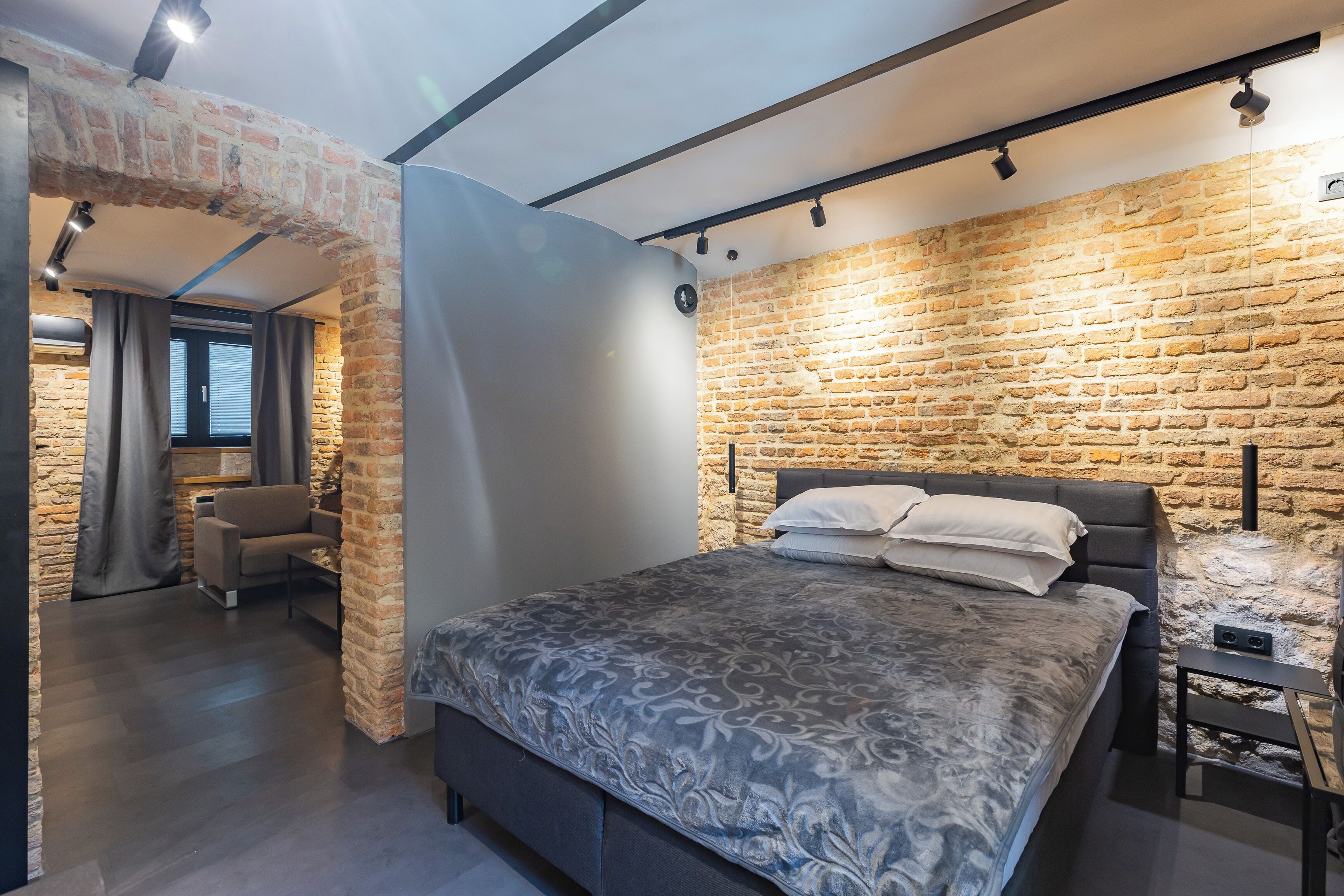 Een moderne slaapkamer met een stenen muur, een bed met beddengoed met een patroon, een bank en een kleine tafel.
