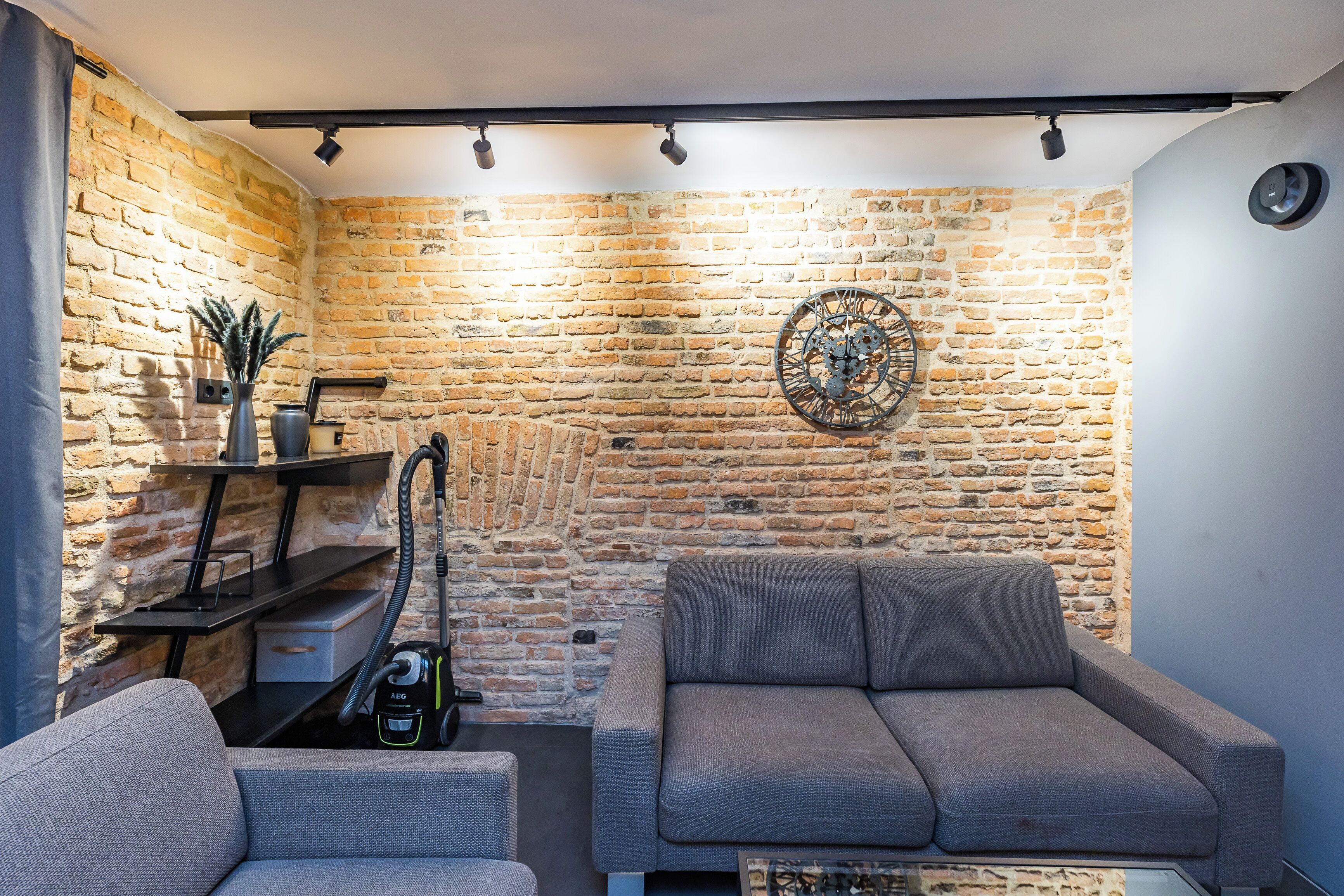 Una sala de estar moderna con una pared de ladrillo, un sofá gris, una mesita y un aspirador.