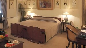 Hotelkamer met een groot bed, twee nachtkastjes met lampen, een bureau met stoel en kunstwerken aan de muur.