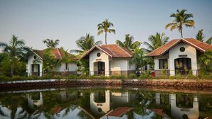 A row of white buildings with red-tiled roofs, a calm water body in the foreground, and palm trees. - Club Mahindra Cherai (Kochi)