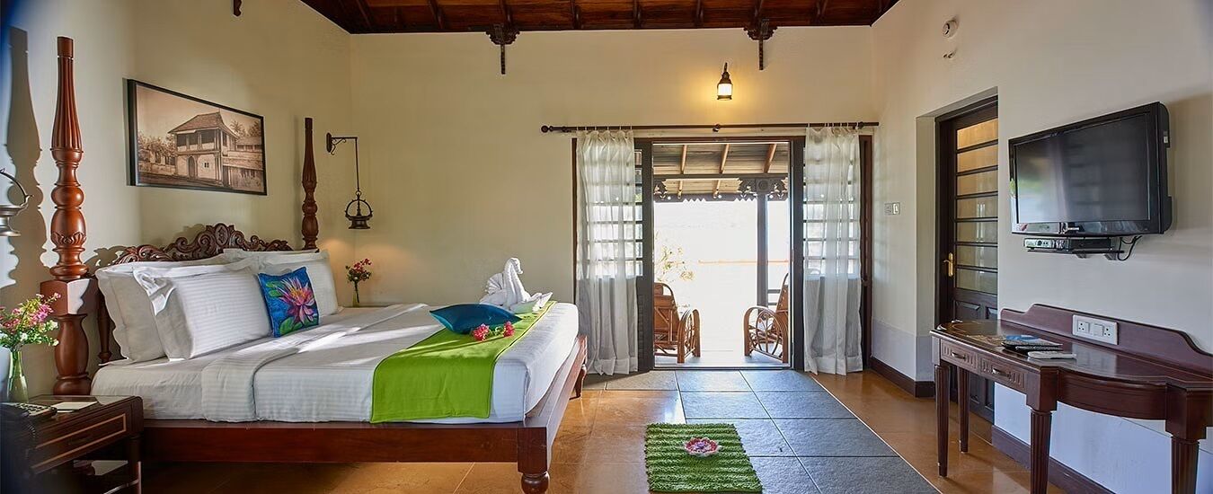 A bedroom with a bed, a desk, a television, and a view to the outside.
