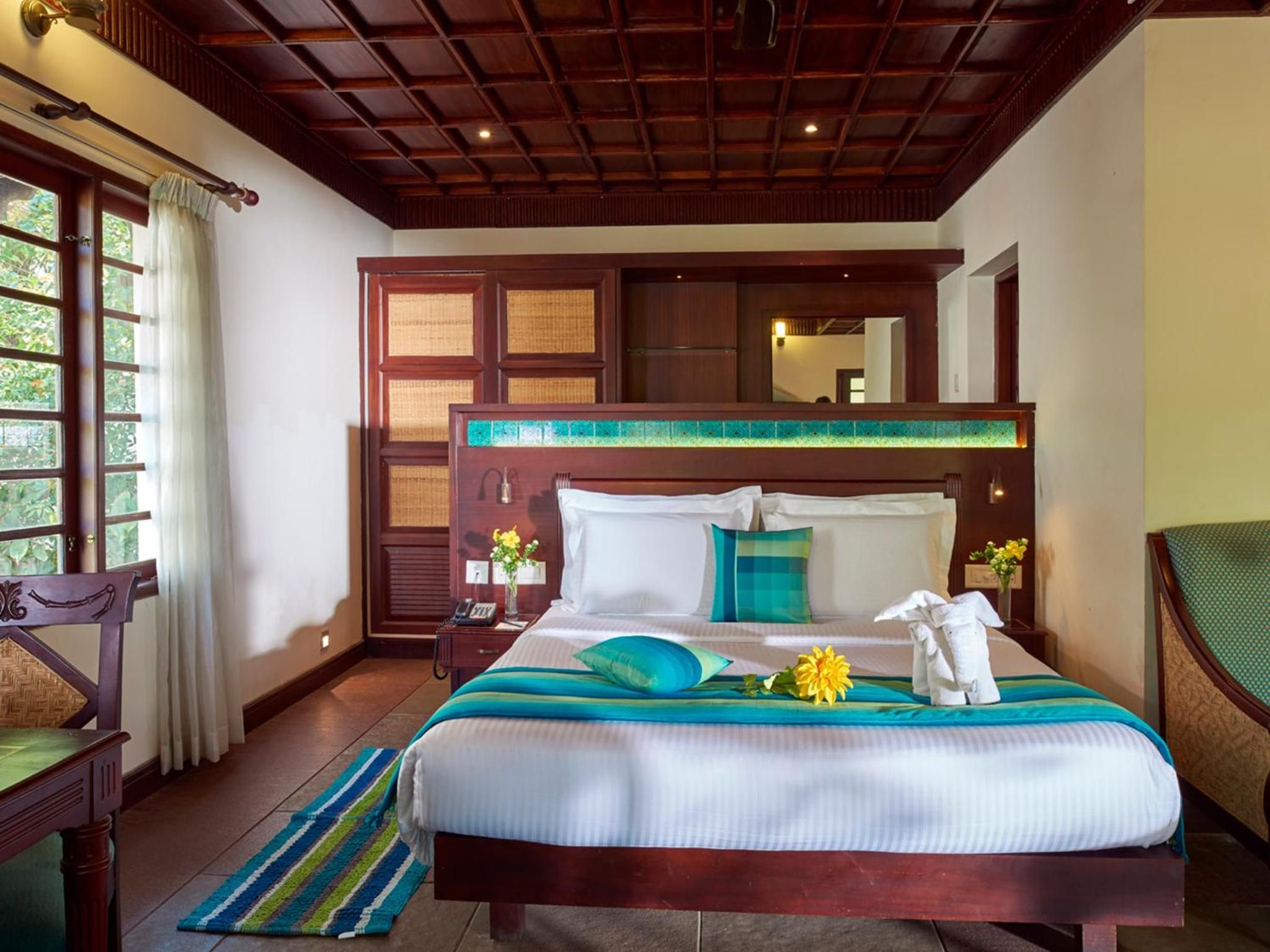 Hotelkamer met een groot bed, een houten hoofdeinde, een nachtkastje met een telefoon, een raam met gordijnen en uitzicht op groen.