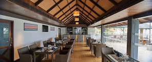 A restaurant with a high ceiling, wooden beams, and a view of the outdoors. - Club Mahindra Cherai (Kochi)