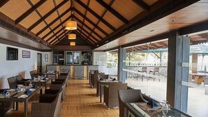 A restaurant with a high ceiling, wooden beams, and a view of the outdoors. - Club Mahindra Cherai (Kochi)