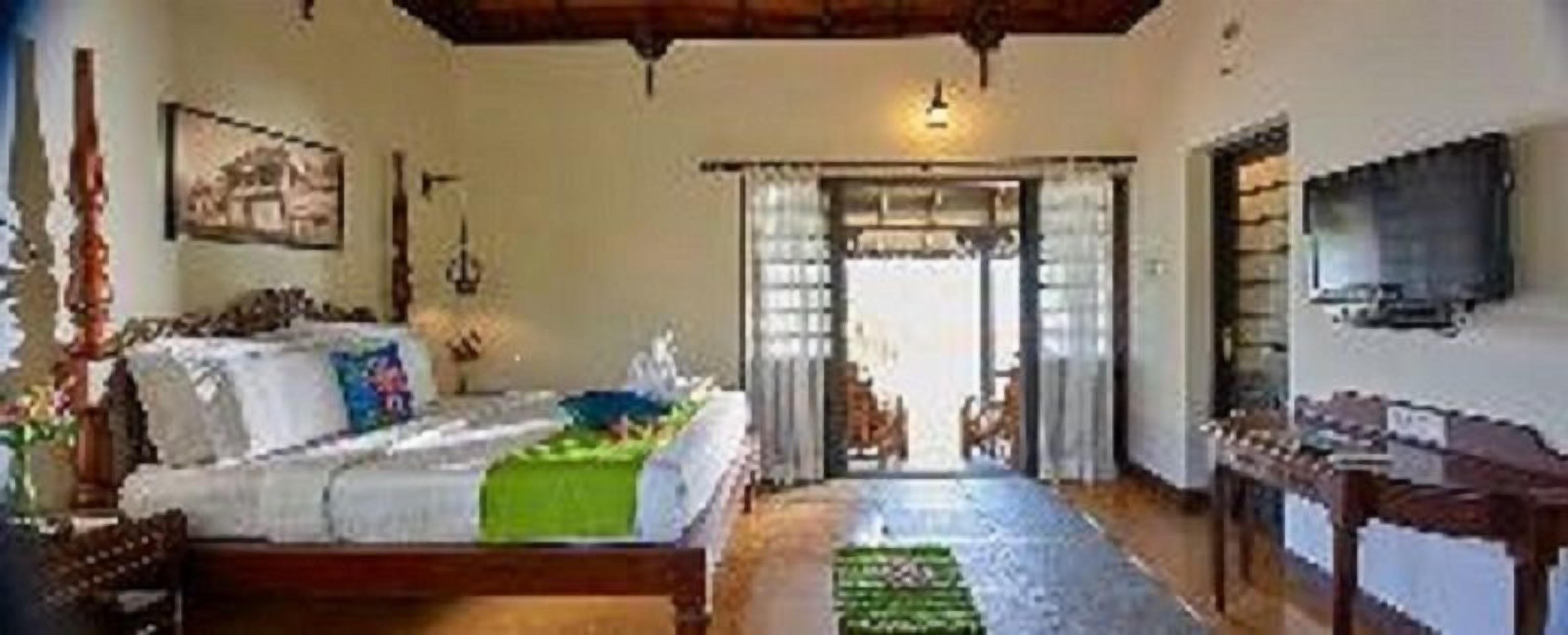 A room with a bed, a television, and a doorway leading to another room.