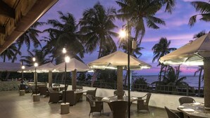 An outdoor dining area with tables and chairs, umbrellas, and palm trees. - Club Mahindra Cherai (Kochi)