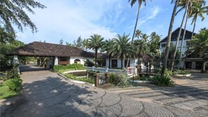 A paved courtyard with palm trees, a covered walkway, and a building with a tiled roof. - Club Mahindra Cherai (Kochi)