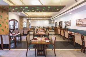 A restaurant with multiple dining tables and chairs, a ceiling with green lights, and artwork on the walls. - Club Mahindra Cherai (Kochi)