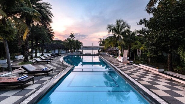 A swimming pool with lounge chairs and palm trees. - Club Mahindra Cherai (Kochi)