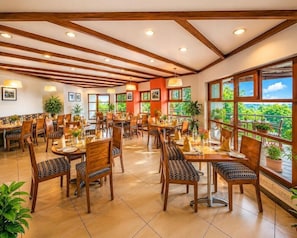 A spacious dining area with multiple tables and chairs, large windows with a view, and wooden ceiling beams. - Sterling Yercaud (Yercaud)