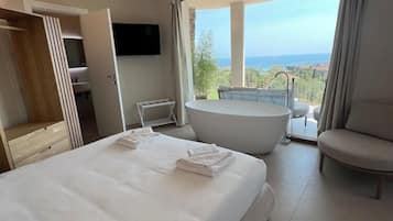 Una camera d'albergo con un letto grande, una vasca da bagno, un'area salotto e un balcone con vista.